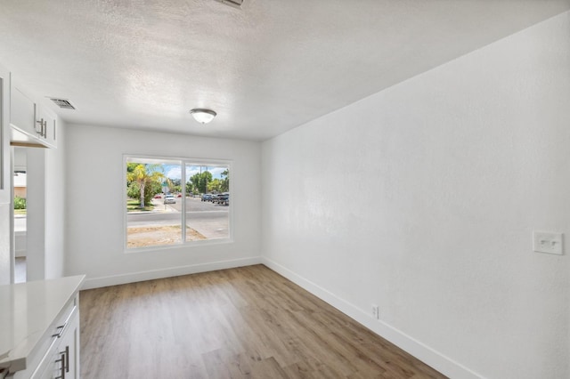 unfurnished dining area featuring a textured ceiling, light wood finished floors, visible vents, and baseboards