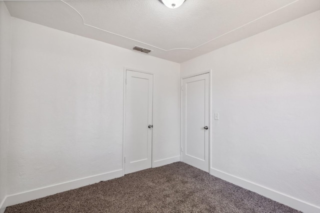 spare room featuring visible vents, dark carpet, a textured ceiling, and baseboards