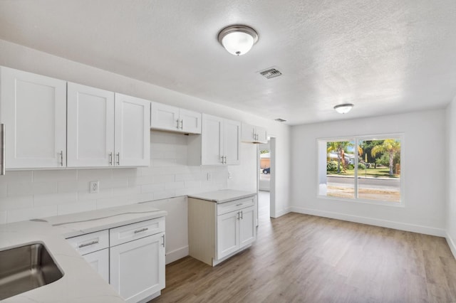 kitchen featuring tasteful backsplash, visible vents, white cabinets, light wood-style flooring, and light stone countertops