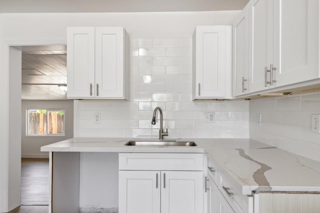 kitchen with tasteful backsplash, a sink, light stone countertops, and white cabinets