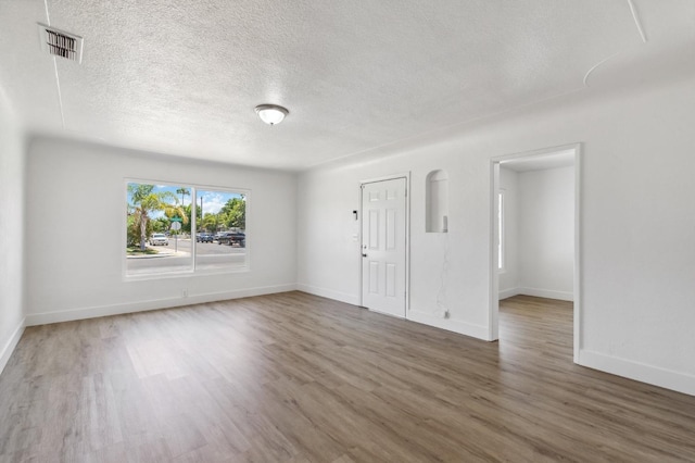 unfurnished room featuring a textured ceiling, wood finished floors, visible vents, and baseboards