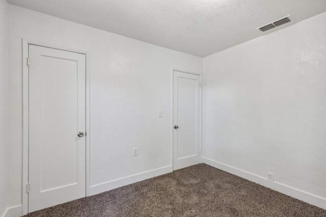 empty room with a textured ceiling, dark carpet, visible vents, and baseboards