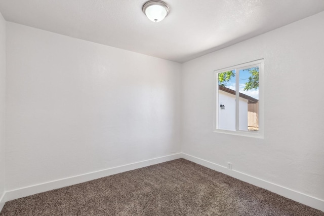 unfurnished room featuring dark colored carpet and baseboards