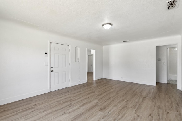 spare room featuring a textured ceiling, baseboards, visible vents, and light wood-style floors