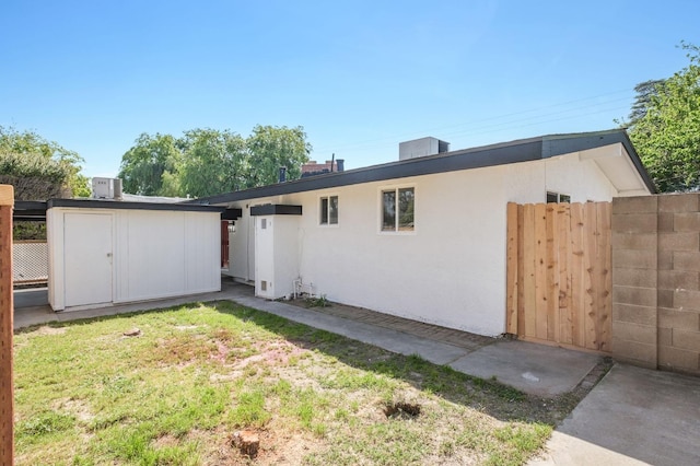 back of house featuring a storage shed, an outdoor structure, fence, and stucco siding