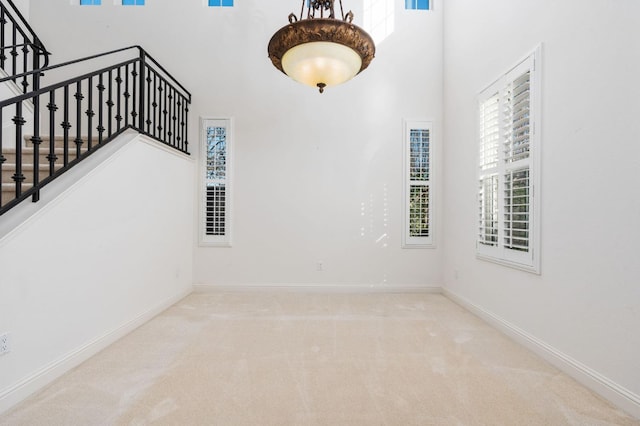 carpeted spare room featuring stairs, a high ceiling, and baseboards