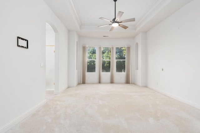 carpeted spare room featuring a tray ceiling, crown molding, arched walkways, and baseboards