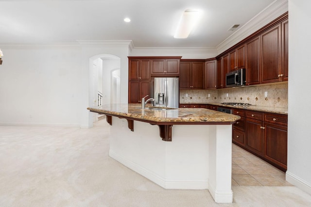 kitchen featuring light stone counters, arched walkways, decorative backsplash, appliances with stainless steel finishes, and a sink