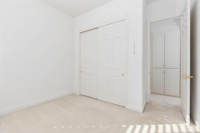 unfurnished bedroom with baseboards, a closet, and light colored carpet