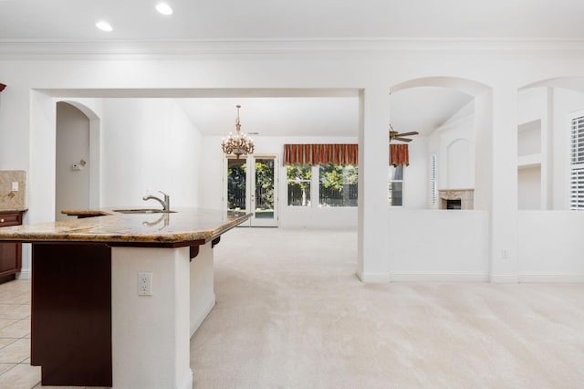 kitchen with light colored carpet, light stone counters, ornamental molding, a sink, and ceiling fan with notable chandelier