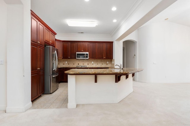 kitchen with arched walkways, decorative backsplash, appliances with stainless steel finishes, light carpet, and light stone countertops