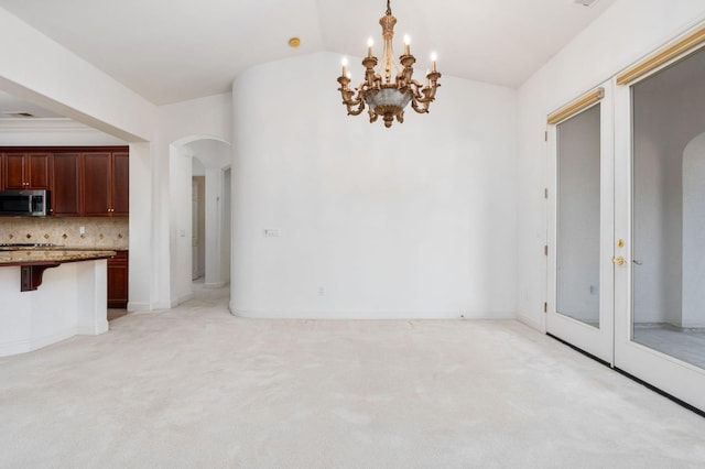 unfurnished dining area featuring baseboards, arched walkways, light colored carpet, lofted ceiling, and a notable chandelier