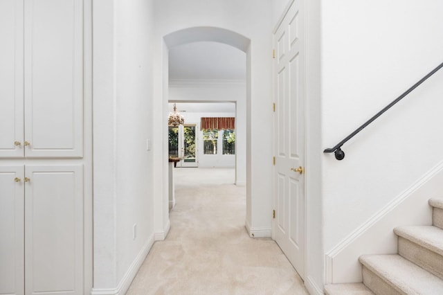 hall featuring arched walkways, light colored carpet, baseboards, stairs, and ornamental molding