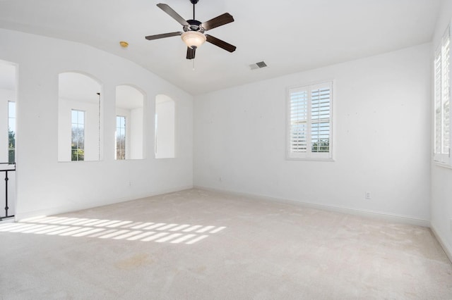 empty room featuring lofted ceiling, light carpet, a ceiling fan, visible vents, and baseboards