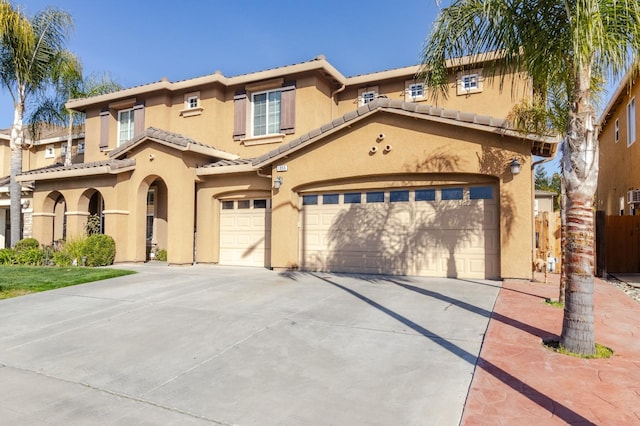 mediterranean / spanish-style house with an attached garage, a tiled roof, concrete driveway, and stucco siding