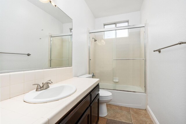 bathroom featuring shower / bath combination with glass door, vanity, toilet, and baseboards