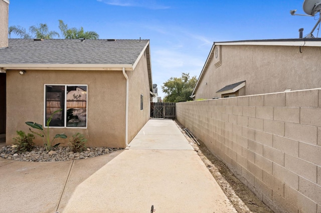 view of property exterior with a shingled roof, fence, and stucco siding