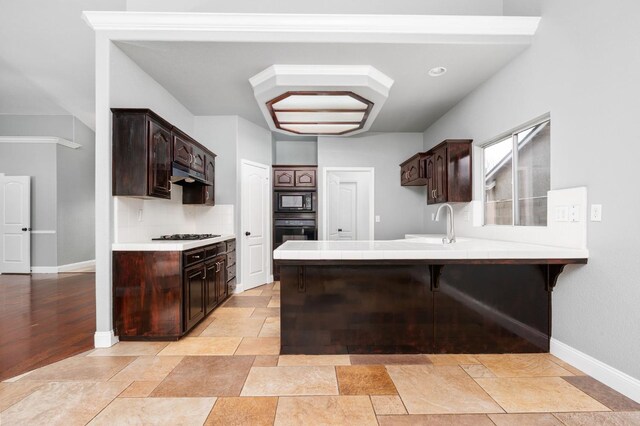 kitchen featuring backsplash, dark brown cabinetry, a peninsula, under cabinet range hood, and black appliances