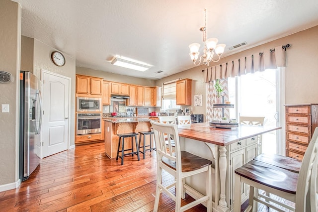 4466 W Artemisa Dr, Fresno, CA 93722 - kitchen with visible vents, appliances with stainless steel finishes, light wood-type flooring, light brown cabinets, and a chandelier
