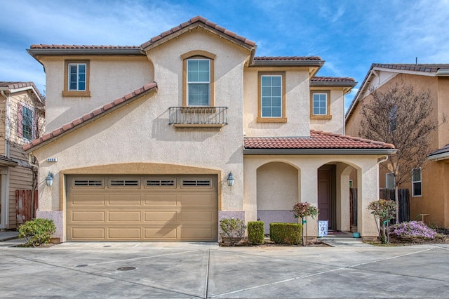 mediterranean / spanish house featuring a tiled roof, an attached garage, and stucco siding