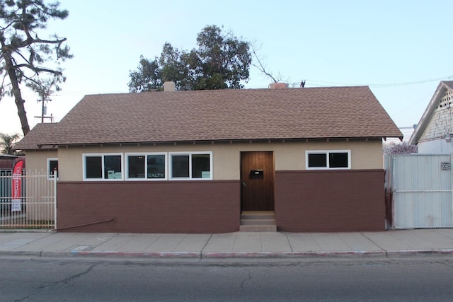 view of front of property with brick siding, stucco siding, roof with shingles, and fence