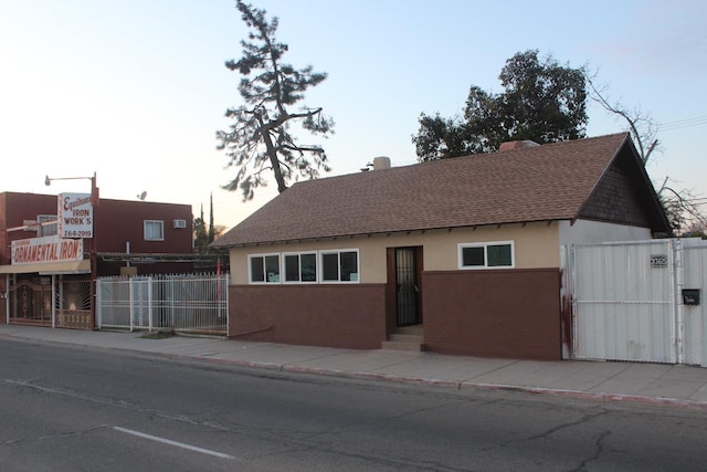 view of front facade with brick siding, fence, roof with shingles, stucco siding, and a gate