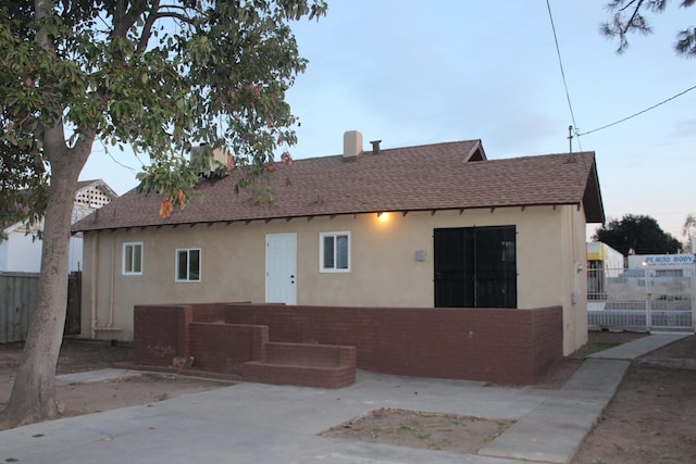 rear view of house with brick siding, stucco siding, roof with shingles, and fence