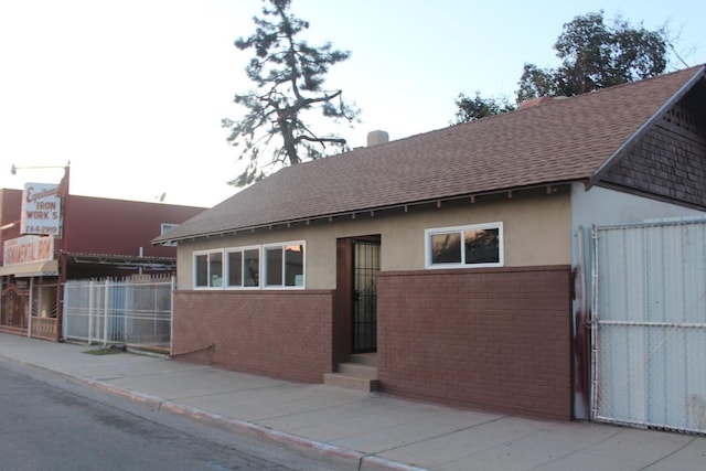 view of front of house featuring stucco siding, fence, brick siding, and a shingled roof