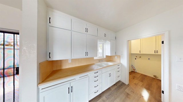 kitchen with light wood finished floors, a sink, light countertops, white cabinetry, and tasteful backsplash