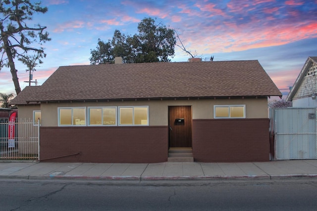 view of front of home with a shingled roof, fence, brick siding, and stucco siding