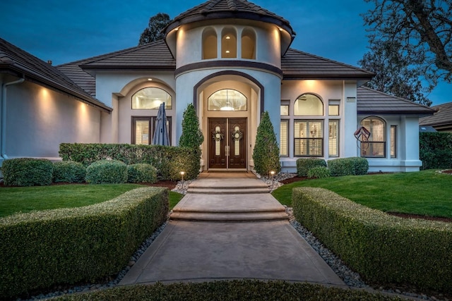 entrance to property featuring french doors, a tile roof, a lawn, and stucco siding