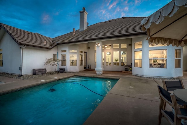 rear view of house with a patio, a chimney, stucco siding, and an outdoor pool