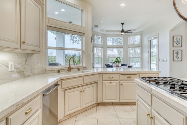 kitchen featuring a tray ceiling, light tile patterned floors, stainless steel appliances, cream cabinets, and a sink