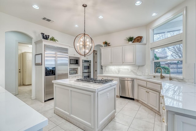 kitchen with arched walkways, visible vents, a kitchen island, a sink, and built in appliances