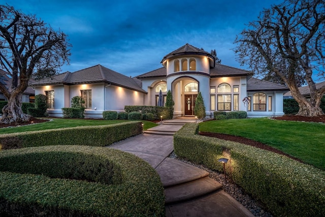 mediterranean / spanish house featuring a front yard, a tile roof, and stucco siding