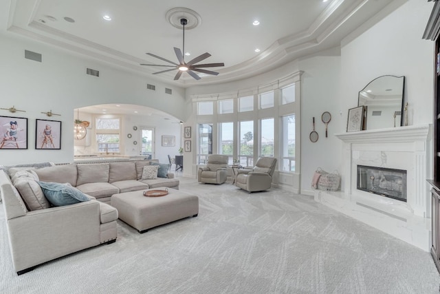 living area featuring arched walkways, a premium fireplace, carpet flooring, visible vents, and a tray ceiling