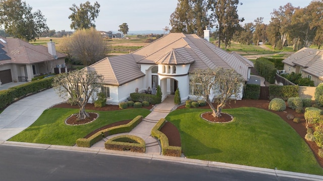 tudor house with driveway, a tiled roof, a front lawn, and stucco siding