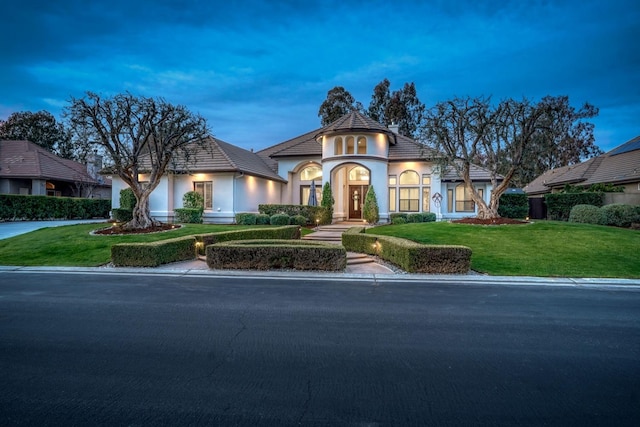 french provincial home featuring driveway, a front yard, and stucco siding