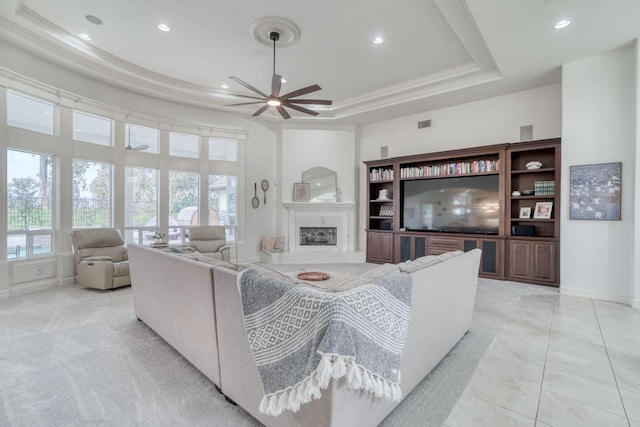 living room featuring a tray ceiling, a fireplace with raised hearth, baseboards, and recessed lighting