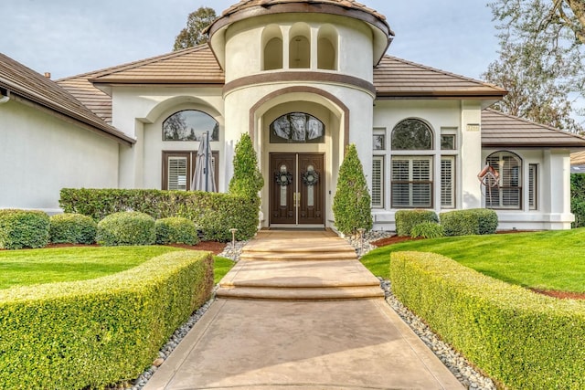 doorway to property featuring french doors, a tile roof, a yard, and stucco siding