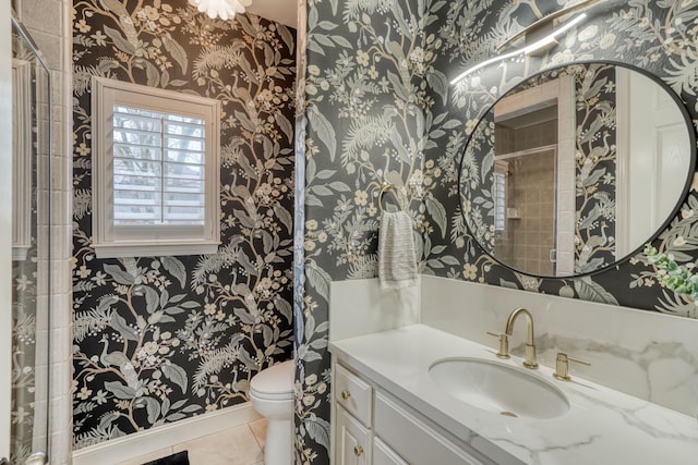 bathroom with wallpapered walls, toilet, vanity, tiled shower, and tile patterned floors