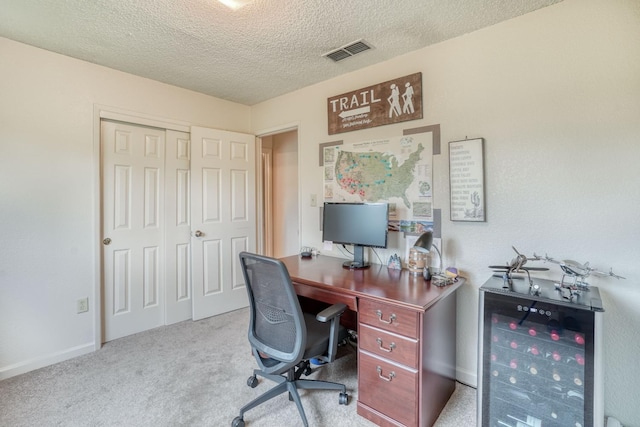 carpeted office space featuring beverage cooler, visible vents, and a textured ceiling