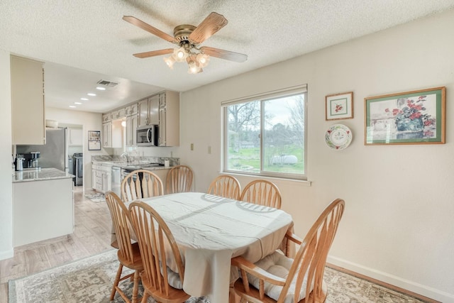 dining room with a ceiling fan, light wood-type flooring, a textured ceiling, and baseboards