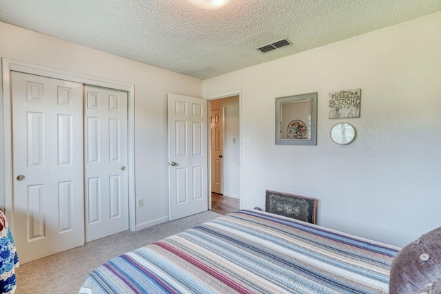 carpeted bedroom featuring a textured ceiling, a closet, and visible vents