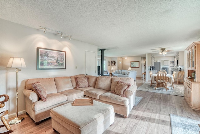 living area featuring light wood finished floors, a ceiling fan, a wood stove, a textured ceiling, and track lighting