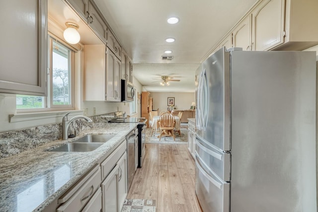 kitchen with light wood-style flooring, stainless steel appliances, a sink, a ceiling fan, and light stone countertops