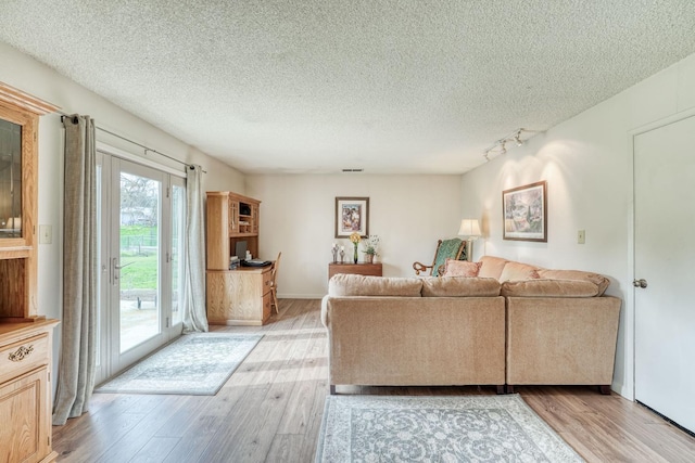 living room featuring a textured ceiling, baseboards, rail lighting, and light wood-style floors