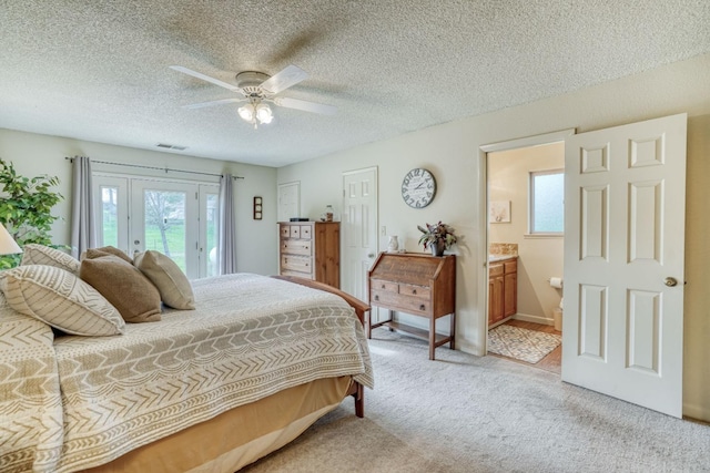 bedroom with ceiling fan, ensuite bathroom, light carpet, visible vents, and access to outside