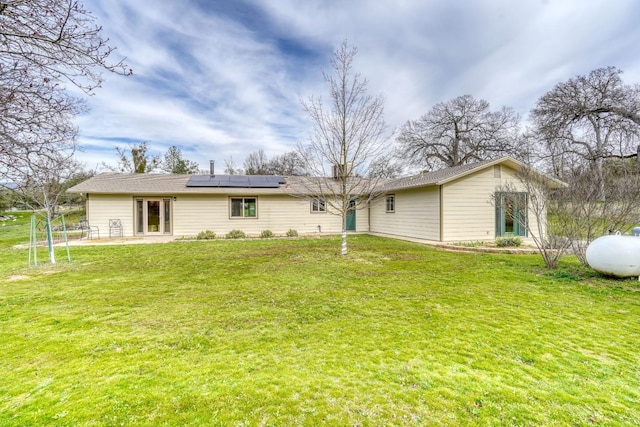 rear view of property with solar panels, a lawn, and a patio