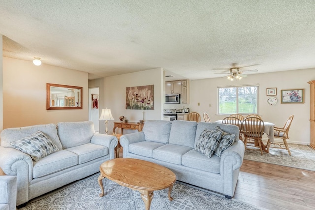 living room with light wood-style floors, ceiling fan, a textured ceiling, and baseboards